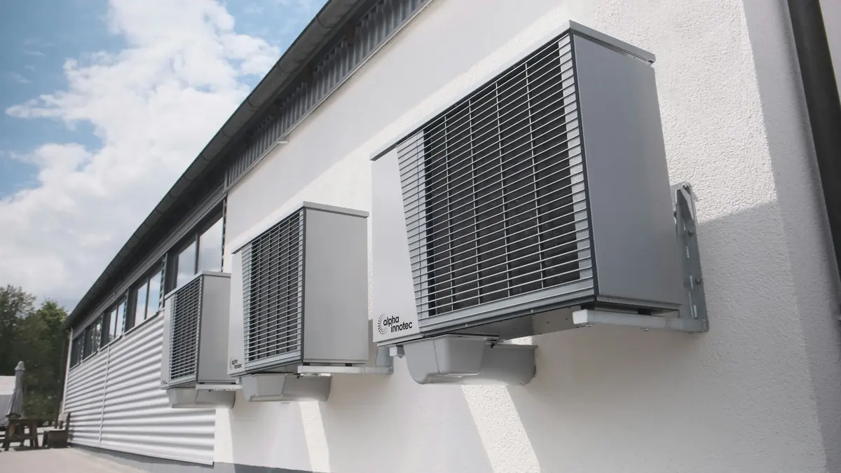 Tres bombas de calor grises instaladas en batería sobre una pared blanca